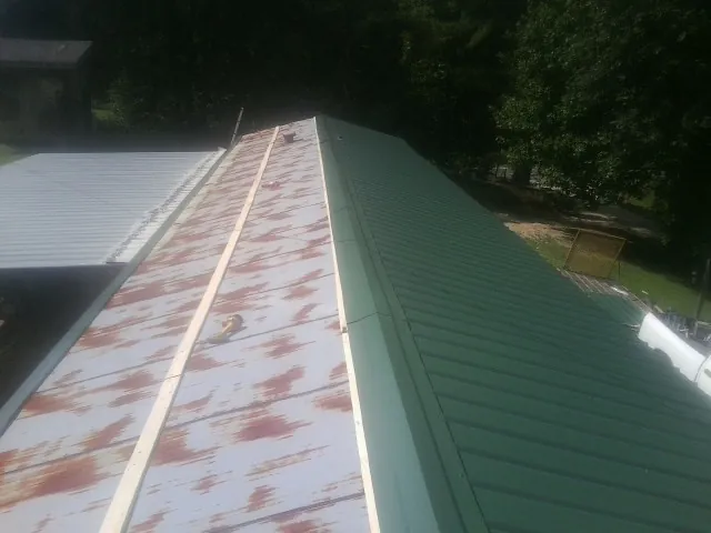 Old rusted panels beside newly installed green metal roofing — Wind Damage Roof Repair by Roofing Brothers in Sylvester