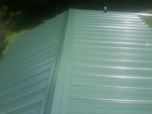 New green metal panels meeting at the ridge of a roof — Flat Roof Repair work by our crew in Sylvester
