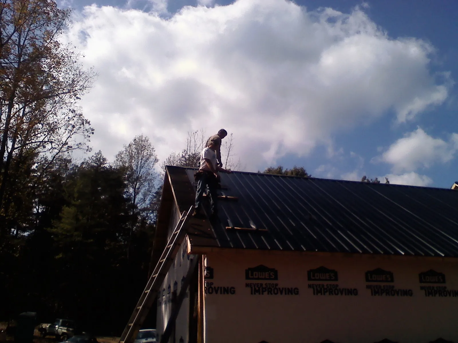 Roofer fastening dark metal panels high against a cloudy sky, from a Roof Inspection job in Sylvester