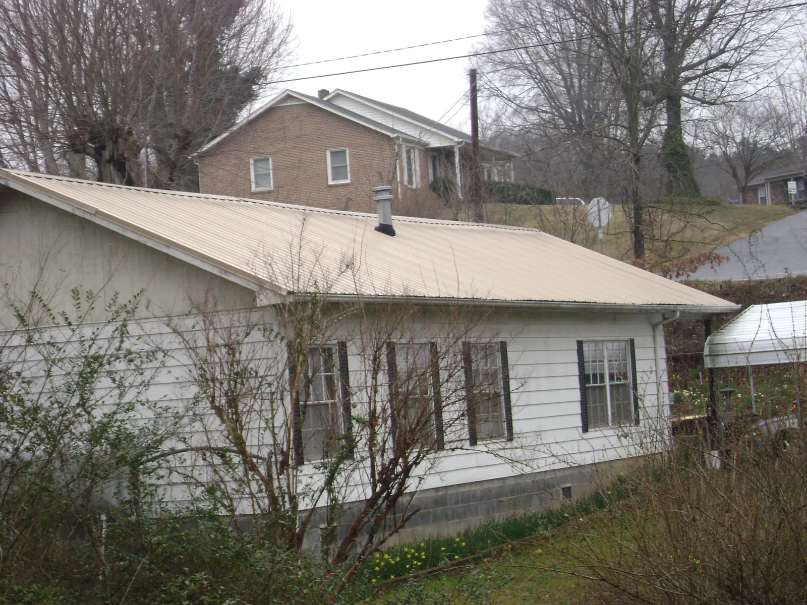 Tan metal roof on a white sided house set into a hillside — Commercial Roofing by Roofing Brothers in Sylvester